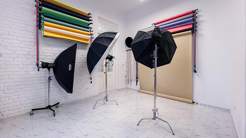 Photography studio interior with lighting equipment, softboxes on stands and colorful backdrop papers mounted on wall.