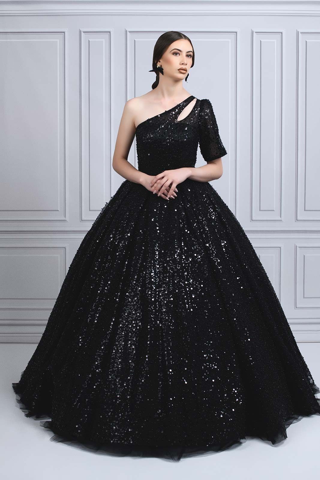 Dramatic black sequined ball gown with one-shoulder neckline and full sparkly skirt photographed in studio setting.