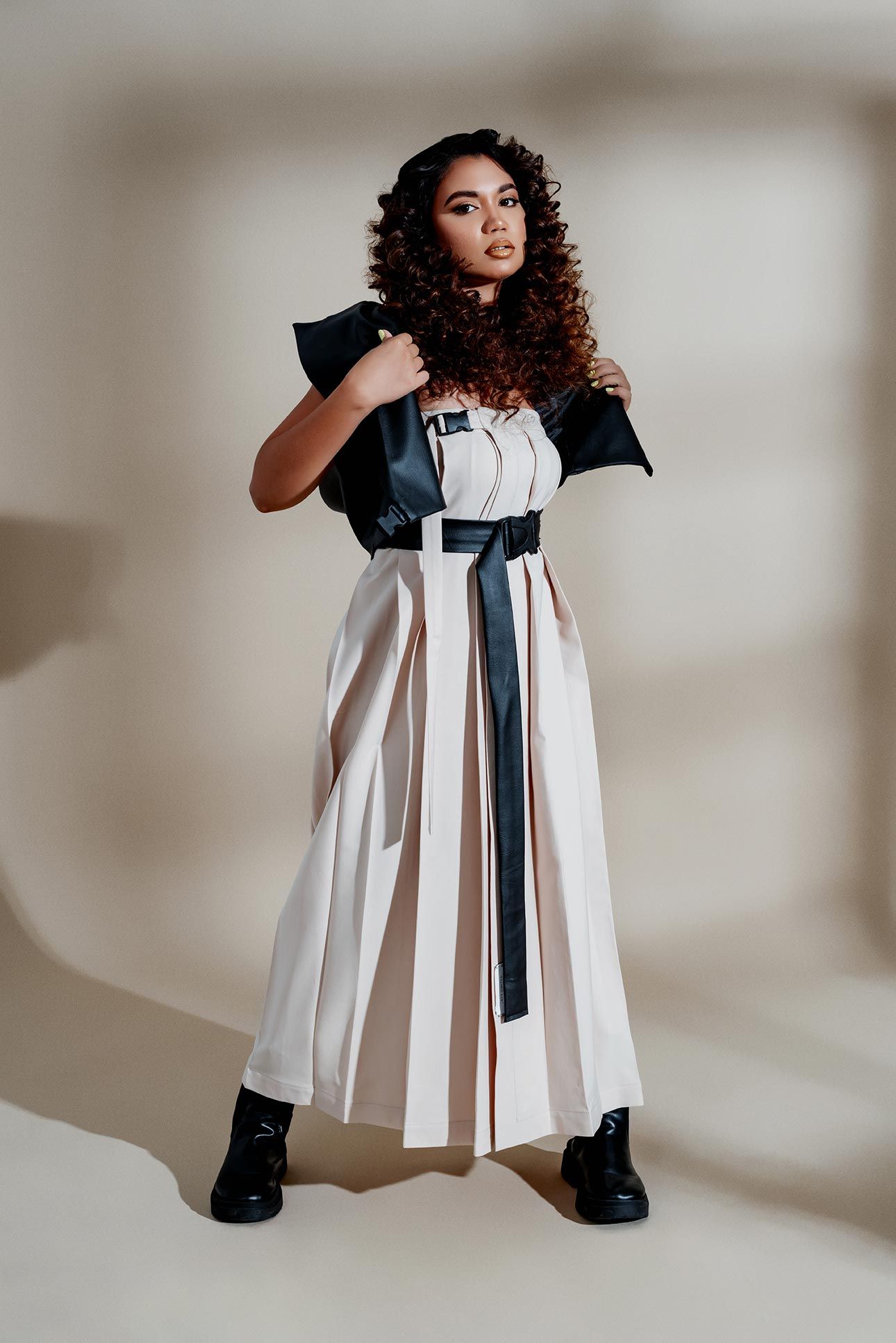 Fashion model in contrasting white dress with black accents strikes confident pose wearing combat boots against neutral backdrop.