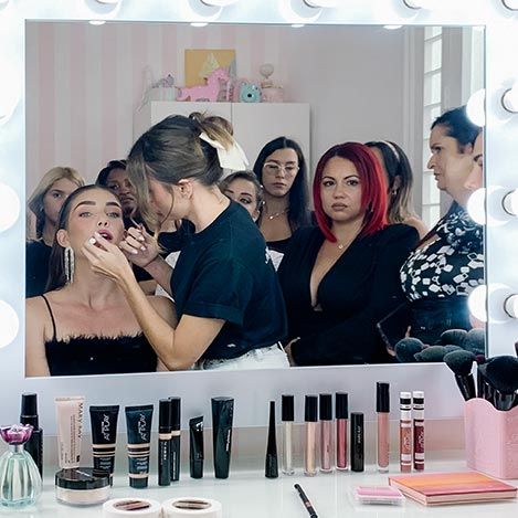 Makeup artist applies cosmetics at beauty station with mirrors and products on counter in professional setting.