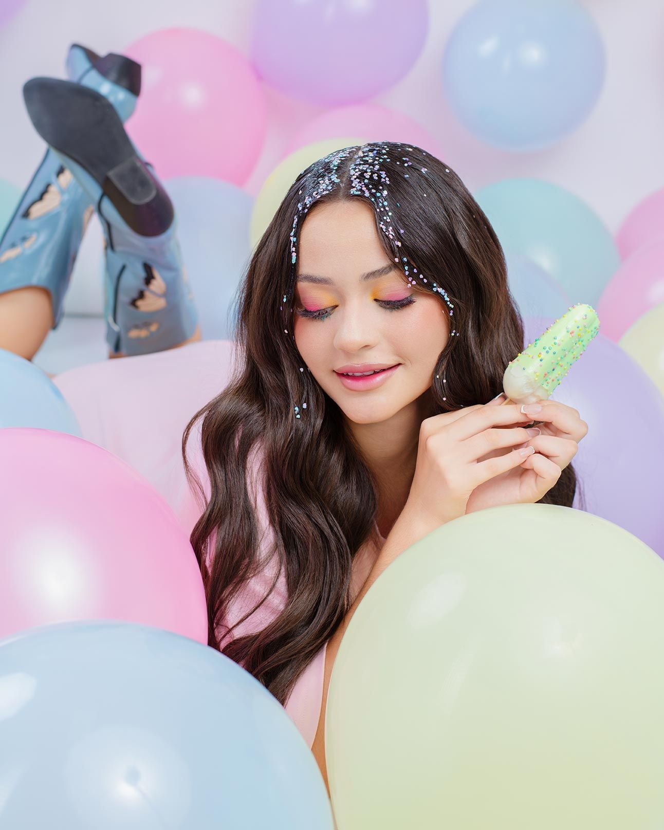 Dreamy portrait surrounded by pastel balloons with sparkly hair accessories in a whimsical setting.