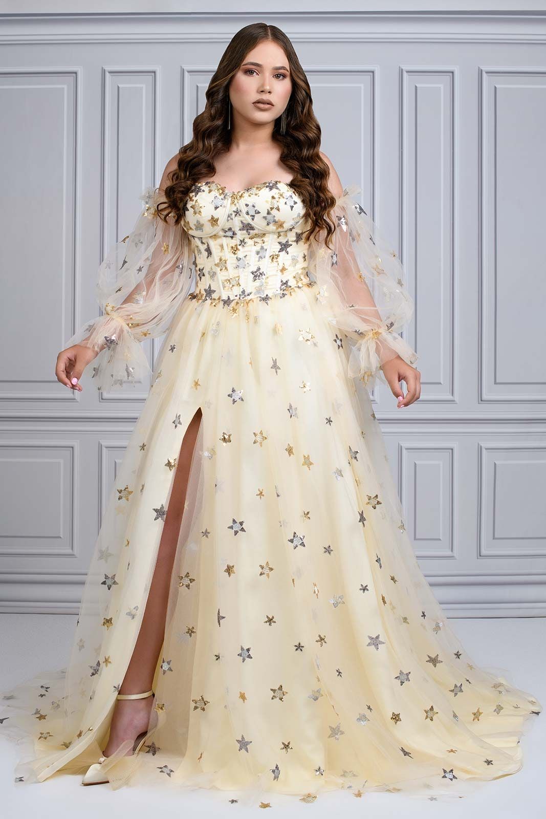 A champagne colored formal gown with star embellishments and sheer sleeves features a feminine sweetheart neckline.