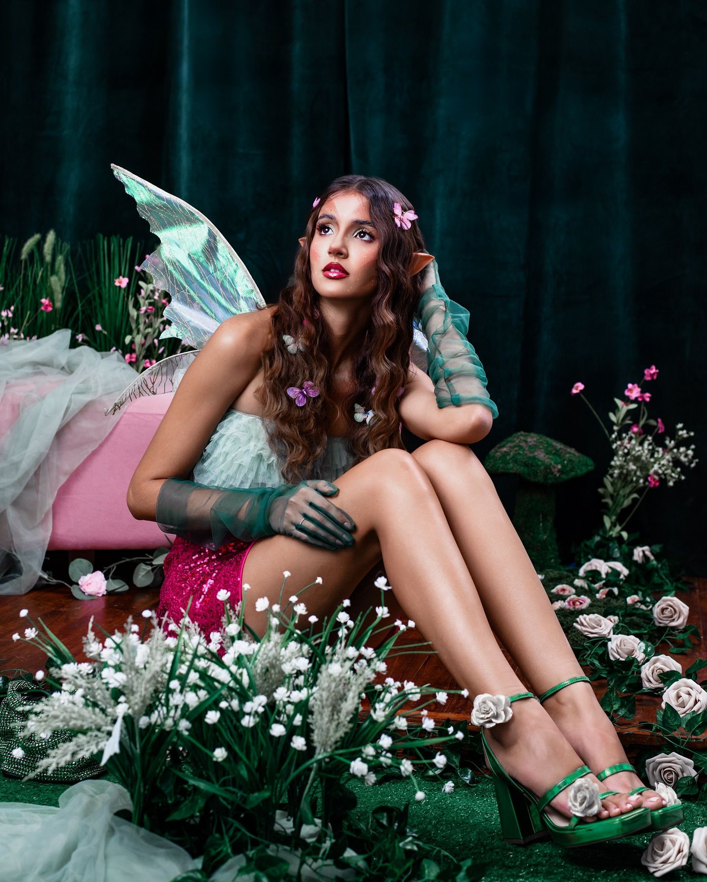 Ethereal fairy-inspired portrait in a lush garden setting with wings, flowers, and dreamy teal backdrop.