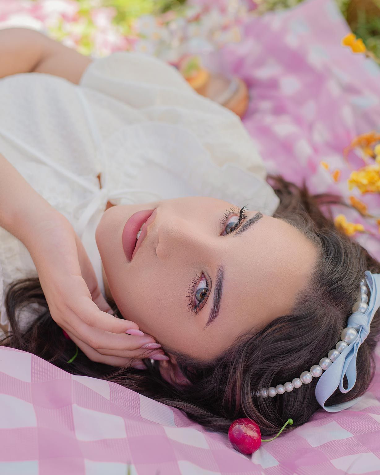 Person lying on pink floral blanket wearing pearl headband and white top with romantic dreamy aesthetic.
