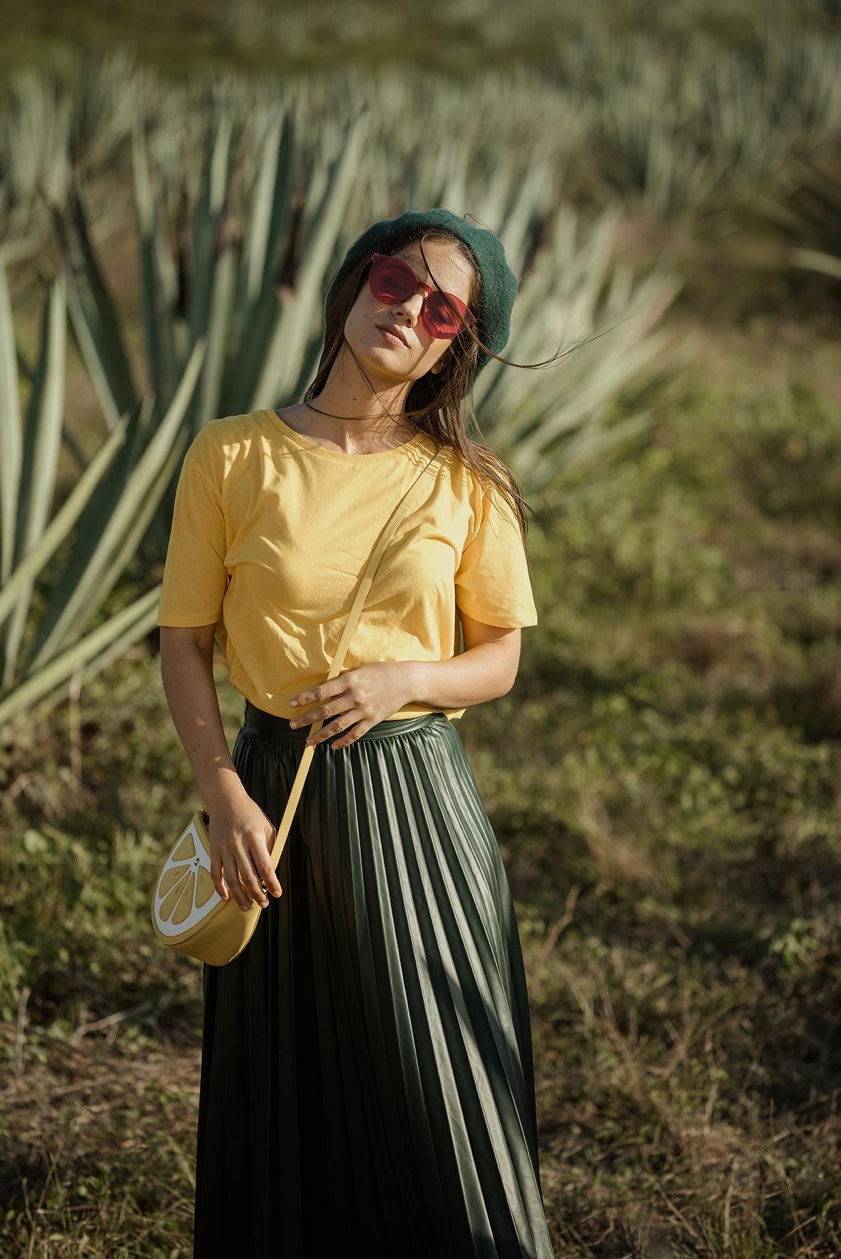 Stylish outfit featuring yellow t-shirt, pleated black maxi skirt and sunglasses against desert landscape with agave plants.
