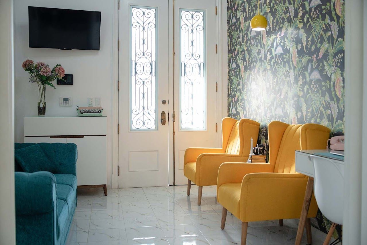 Modern waiting room with yellow armchairs, teal sofa, and decorative wall art next to white doors with glass panels.