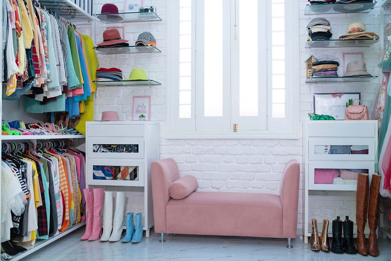 Walk-in closet with pink sofa, white shelving units, and organized clothing collection.