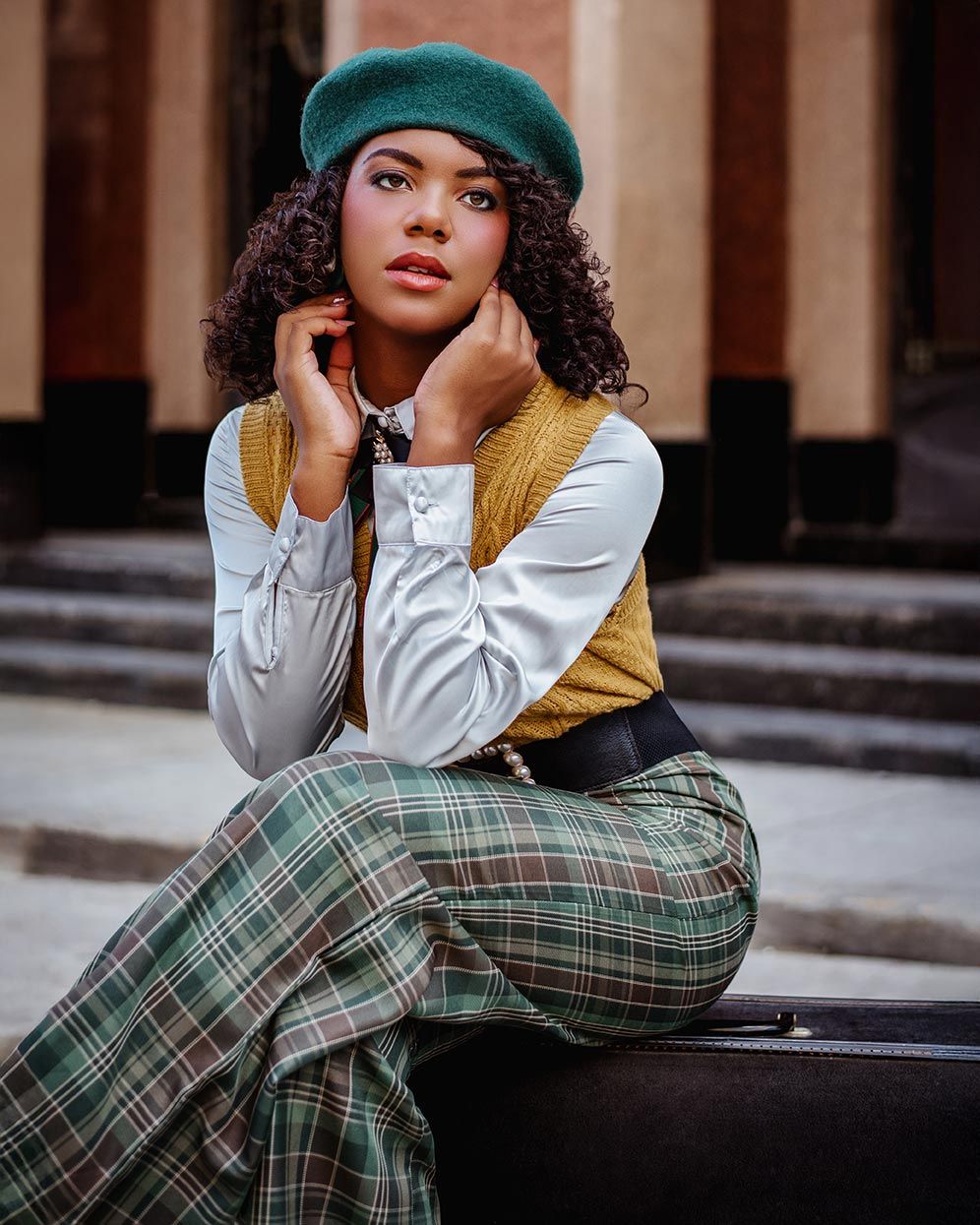 Fashion model in turquoise beret, plaid pants and white blouse posing on steps with vintage-inspired autumn styling.