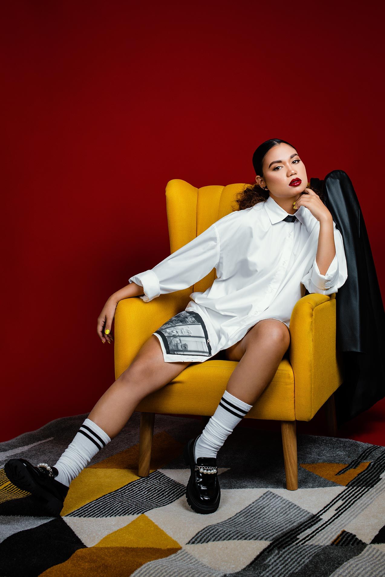 Stylish outfit featuring white shirt dress and knee socks on yellow chair with geometric pattern rug.