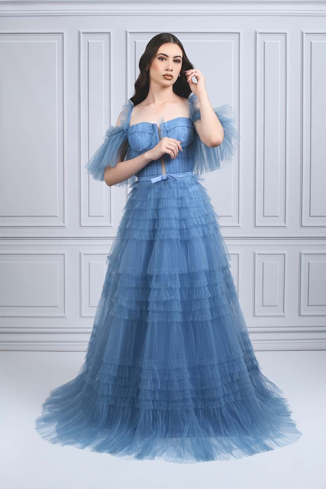 A layered tulle blue ballgown with off-shoulder design and ruffled tiers photographed in a studio setting.
