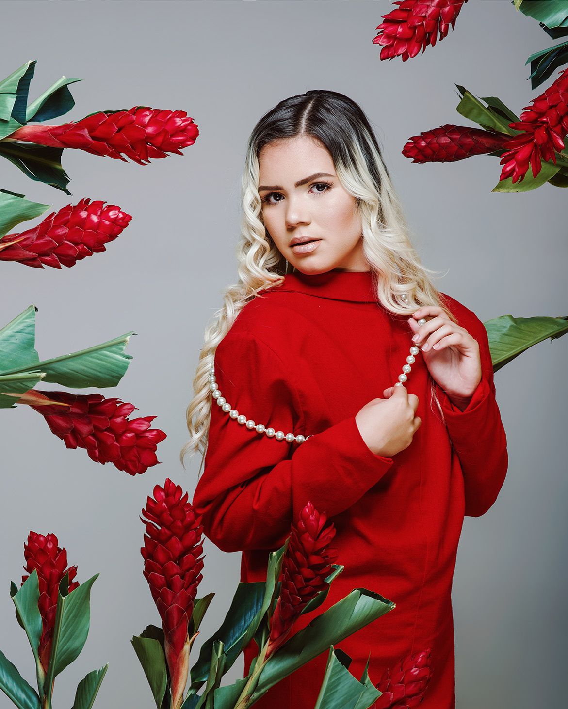 Fashion photo with bright red sweater against gray background surrounded by decorative red ginger flowers.