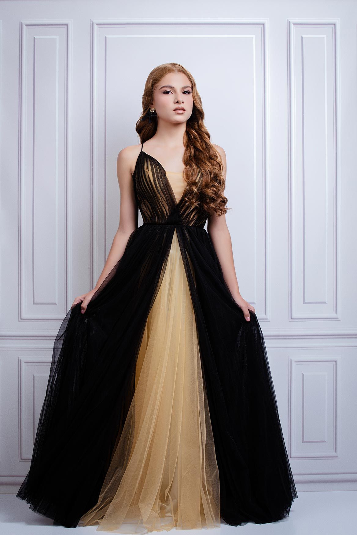 Elegant full-length gown featuring black tulle overlay with plunging neckline and champagne-colored underlay in classic setting.