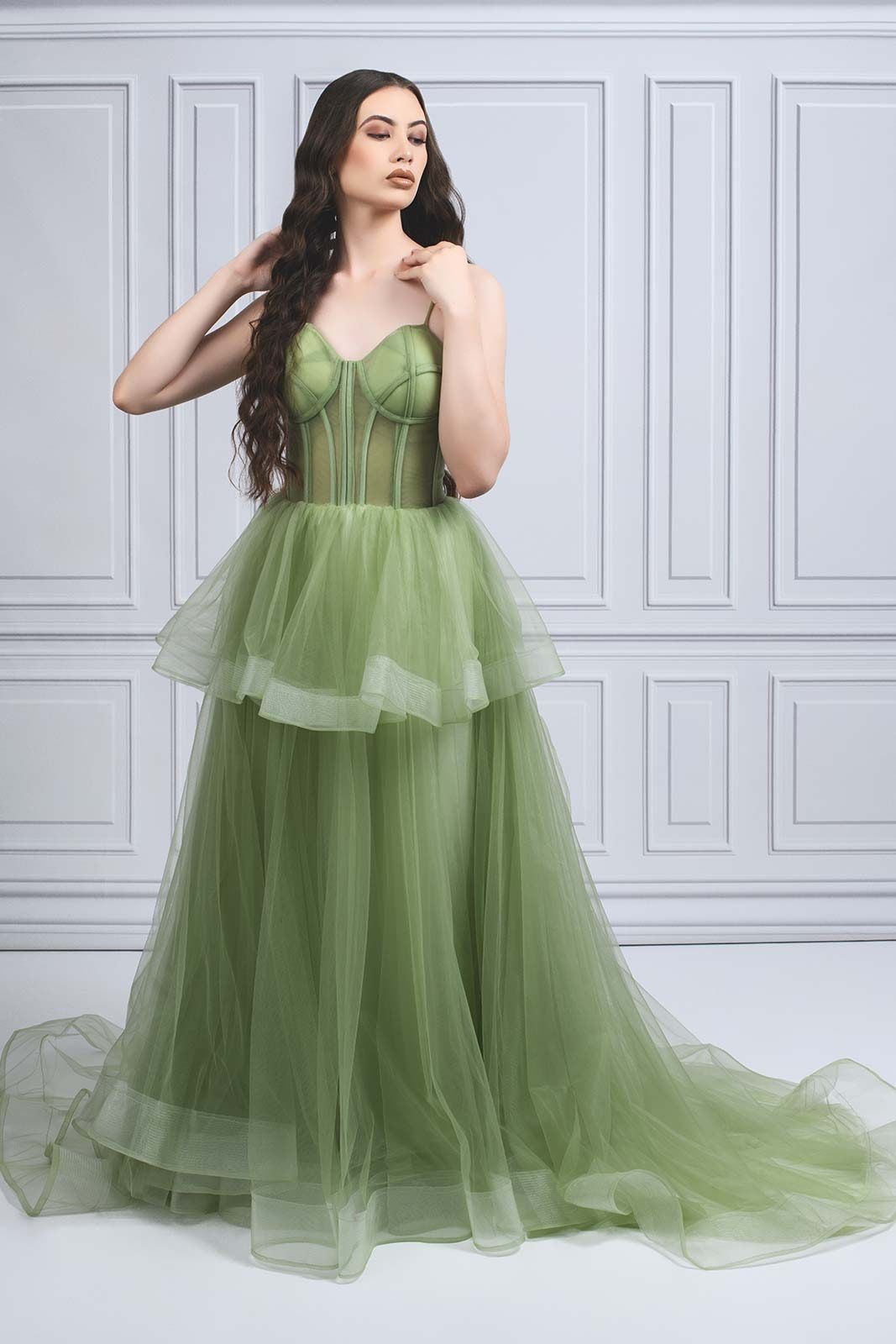 A green tulle ball gown with corset bodice and layered skirt photographed against a white paneled wall.