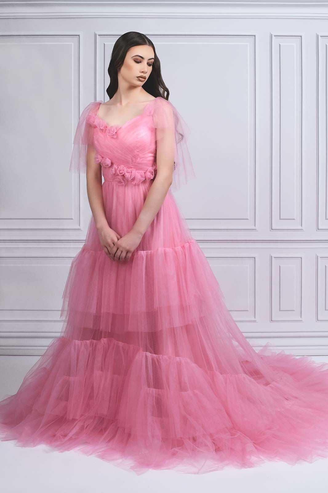 Elegant pink tulle evening gown with sweetheart neckline and flowing train against white paneled wall.