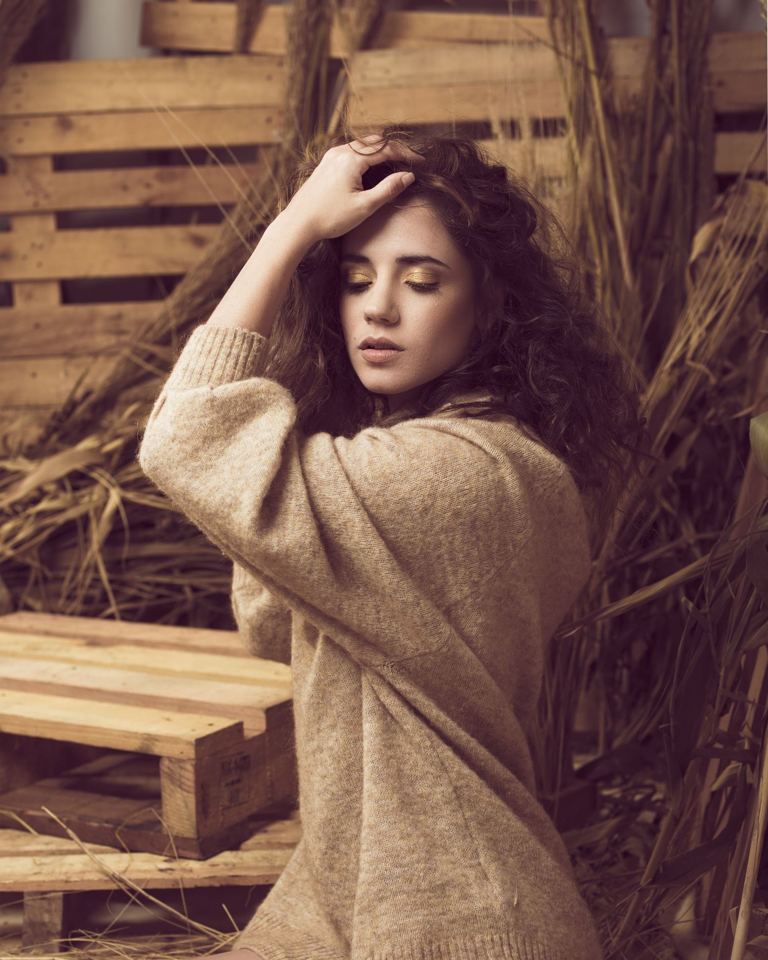 Artistic sepia portrait featuring wavy dark hair and cozy beige sweater against a rustic wooden background.