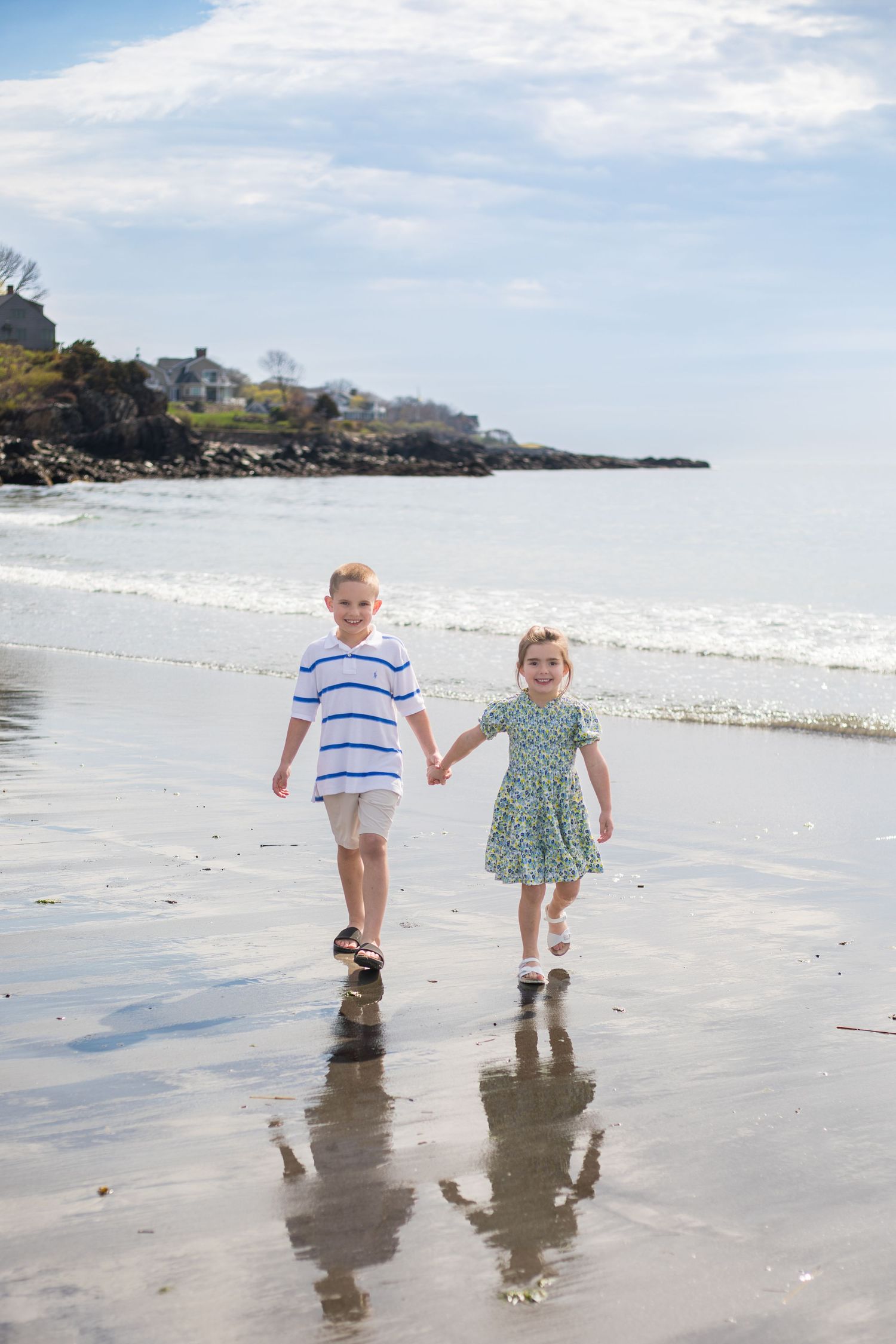 Young brother and sister walk hand in hand on the beach.