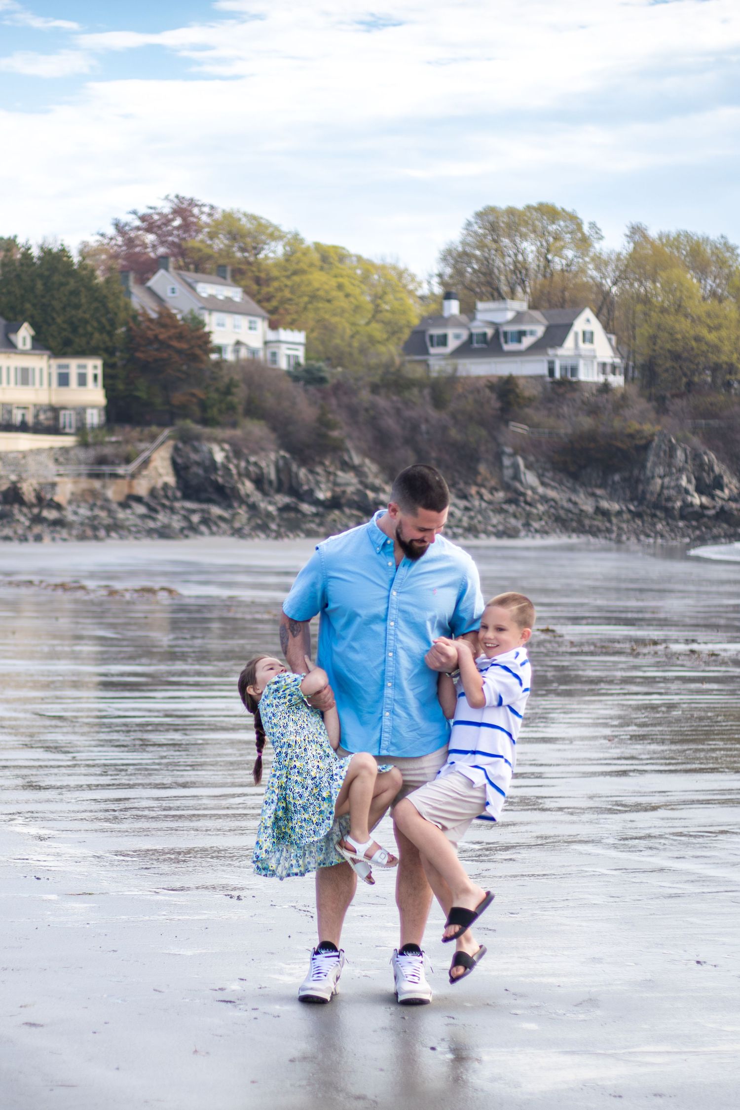 Son and daughter hang on their dad's arms while laughing and playing on the beach.