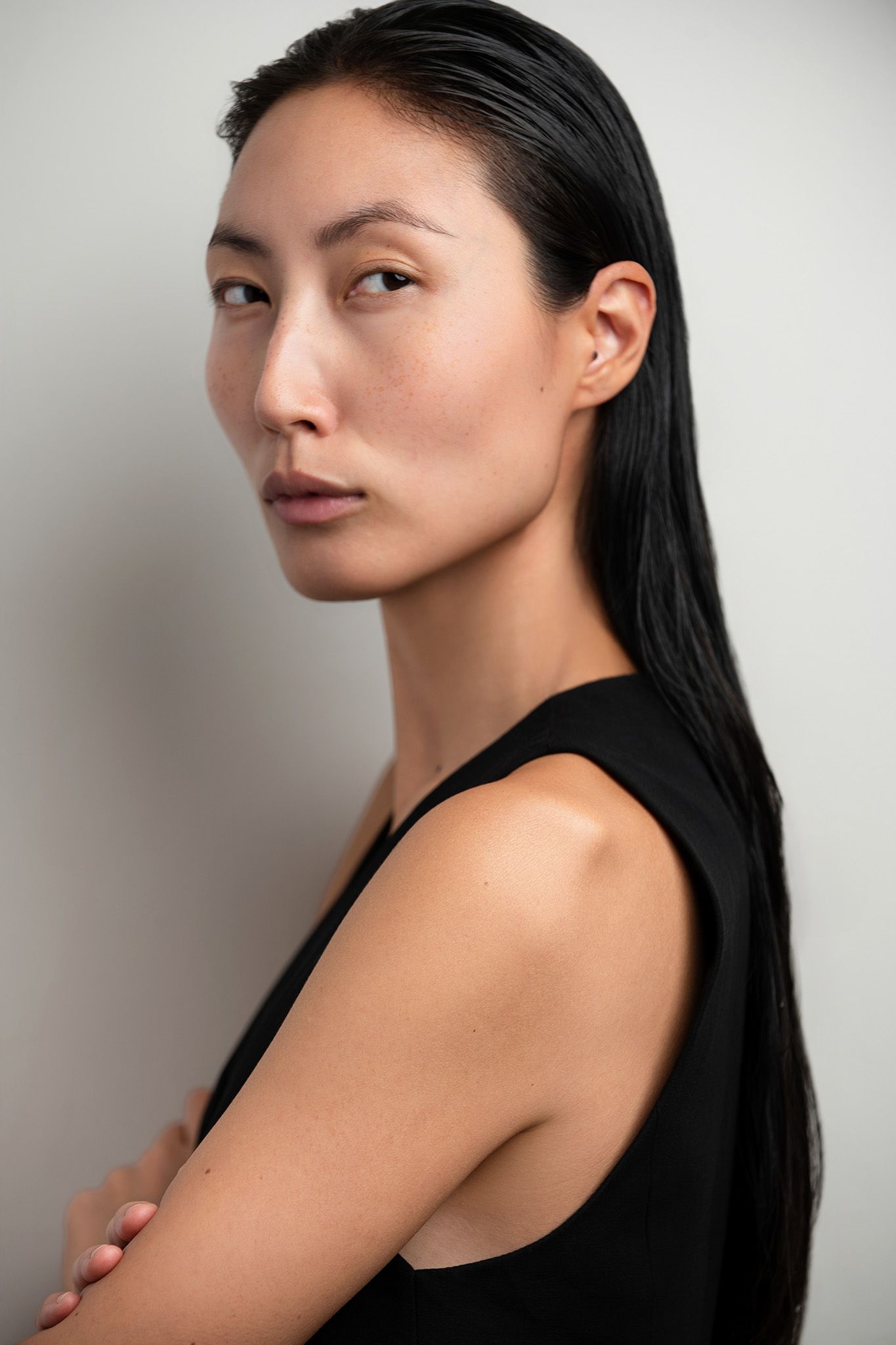 A young Asian woman with sleek black hair poses in a black sleeveless top against a light gray background.