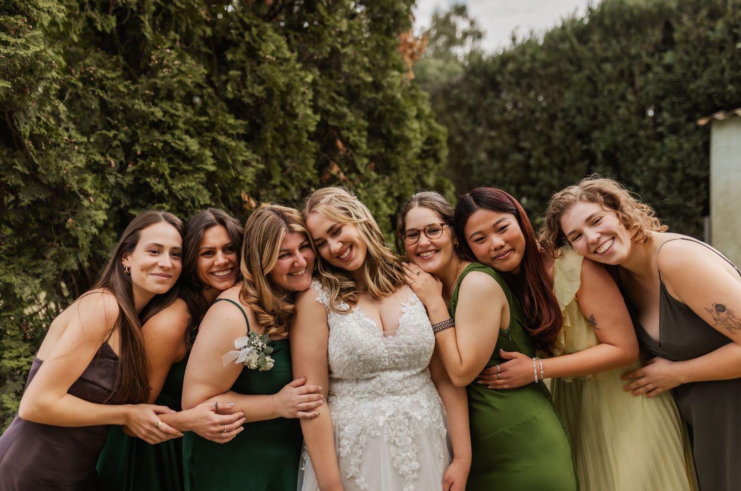 A group of bridesmaids in different colored dresses share a fun candid moment together at an outdoor wedding.
