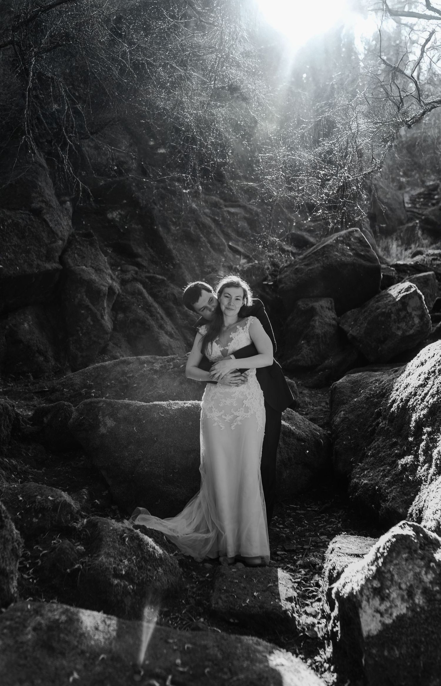 Black and white series of photographs showing a figure in a flowing dress posing near a rocky stream in a mystical forest setting.