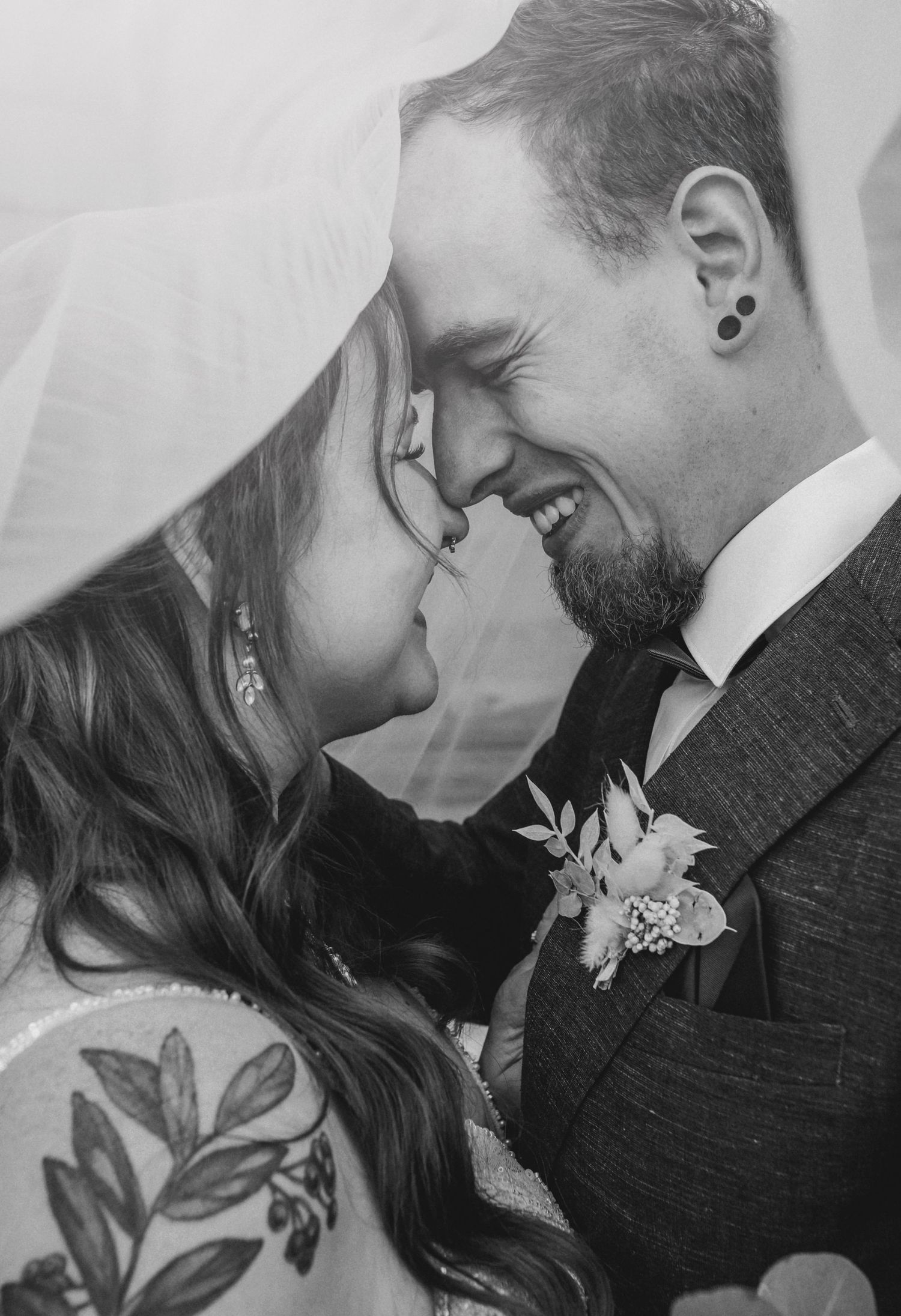 Black and white intimate wedding portrait showing close nose-to-nose romantic moment with bride's veil and floral boutonniere.