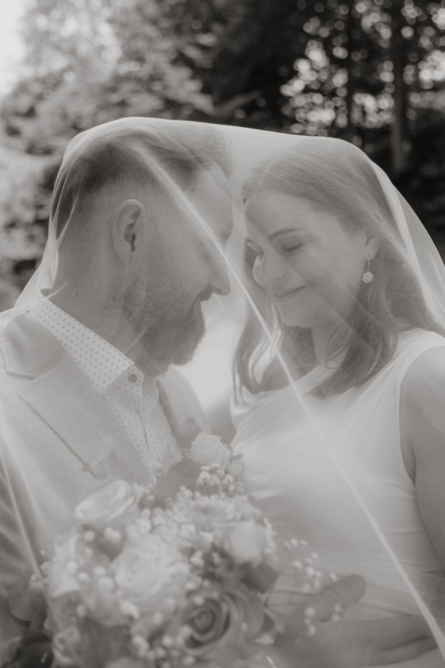 A romantic black and white photo sequence of a wedding couple kissing under a delicate veil with white flowers.