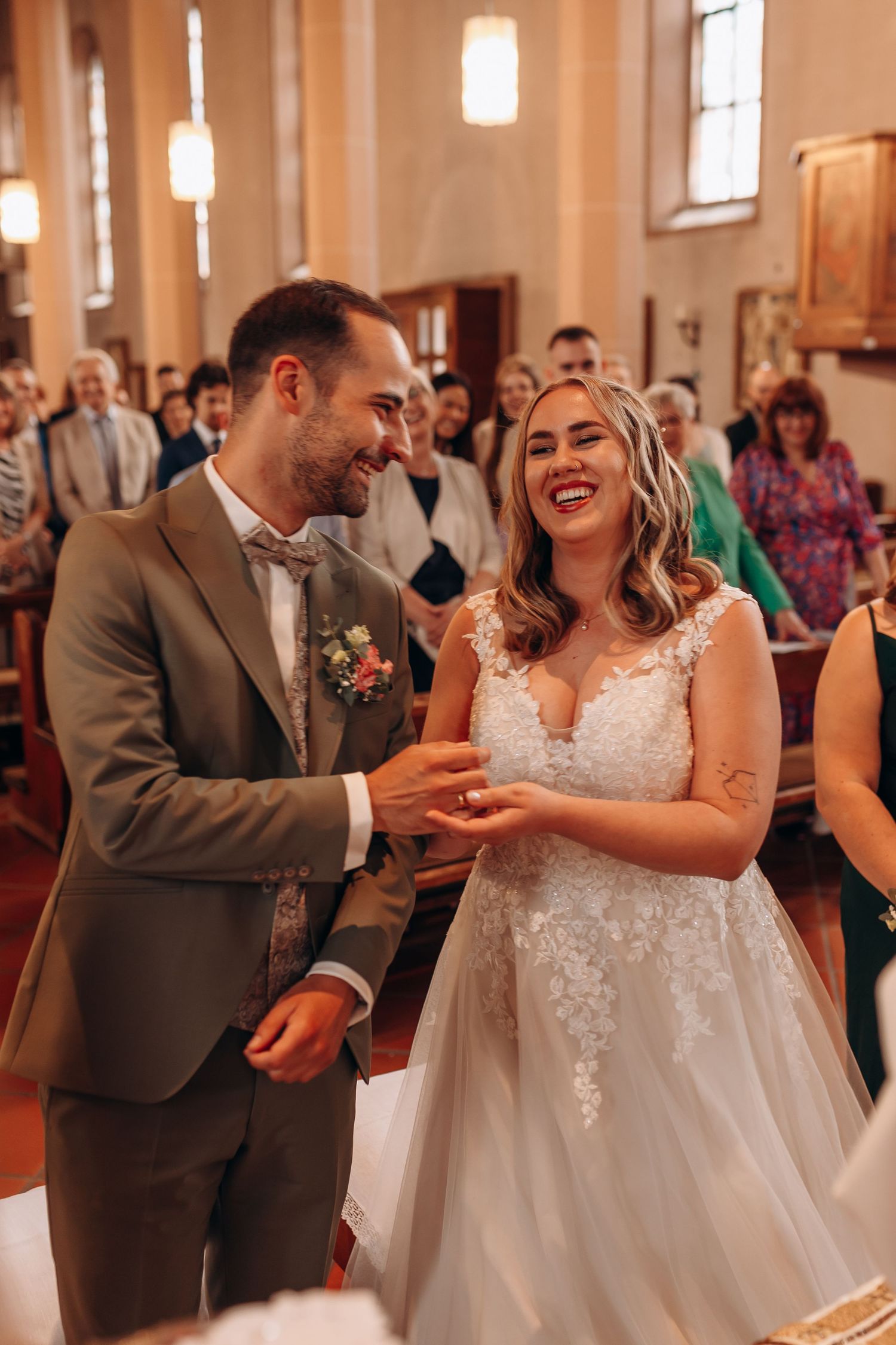 A delighted couple shares a joyful moment during their wedding ceremony inside a warmly lit church sanctuary.