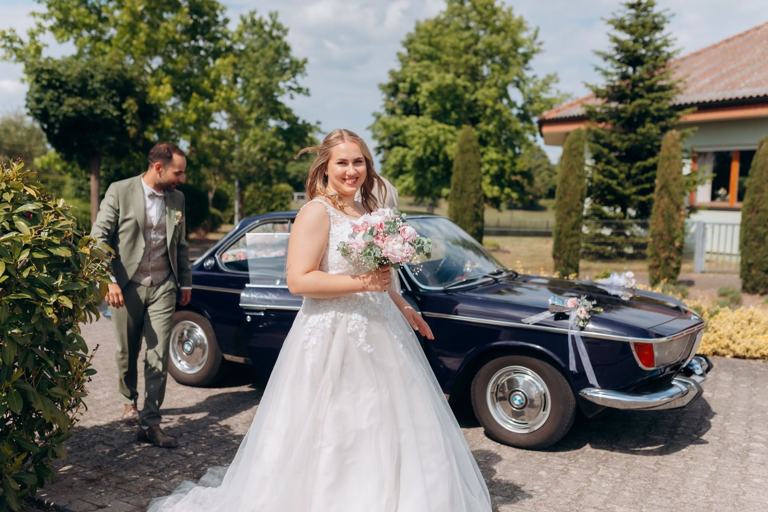 A classic dark blue vintage car decorated with flowers serves as an elegant backdrop for a beautiful wedding celebration.