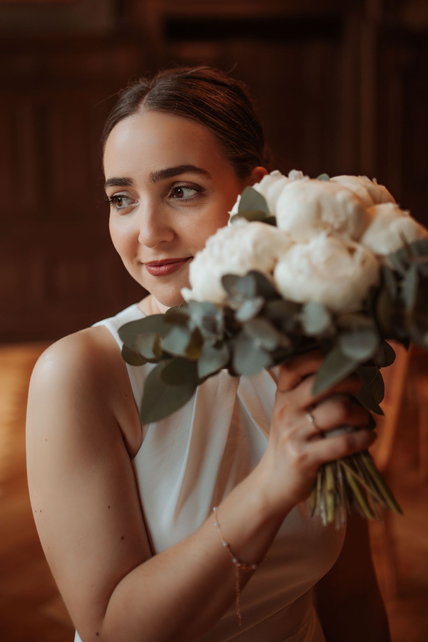 Bride in sleeveless white dress holding romantic bouquet of white peonies and eucalyptus.