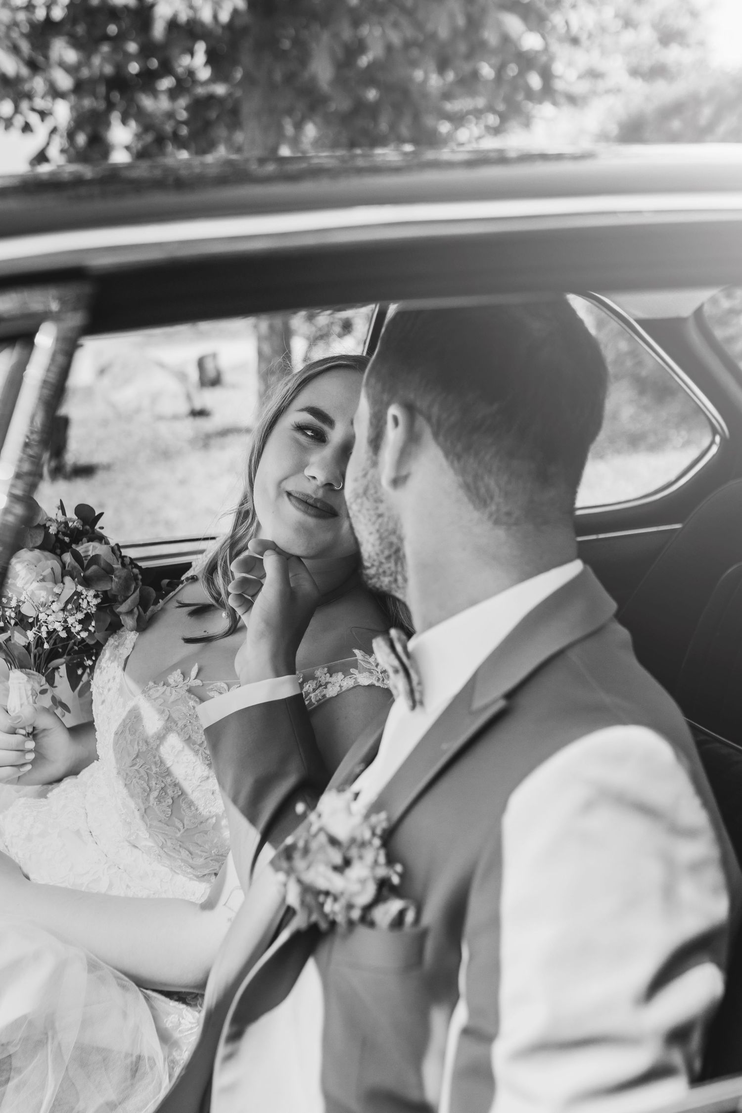 A romantic black and white wedding photo shows a tender moment between newlyweds in the back seat of a car.