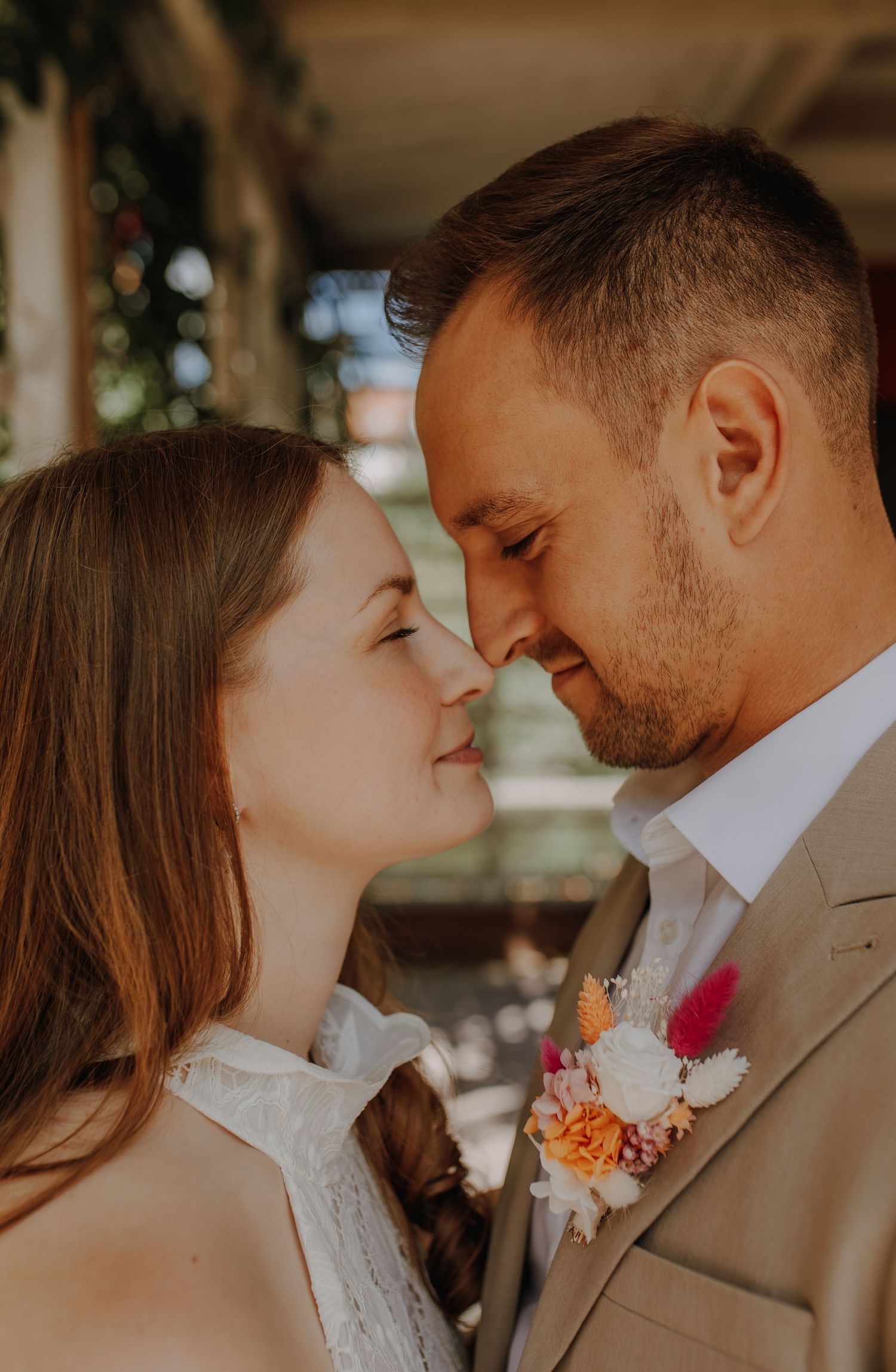 A romantic wedding couple sharing an intimate moment in warm sunlight with peach-colored floral boutonniere details.