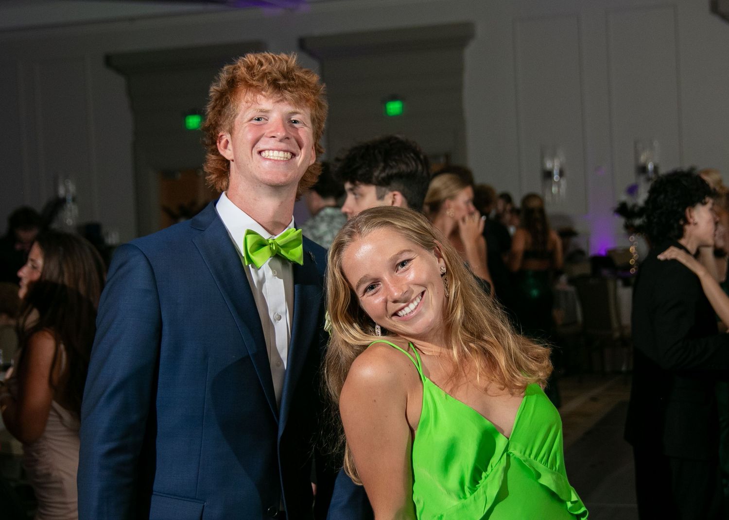 A couple in formal attire dance together at an event, with the woman wearing a bright neon green dress.