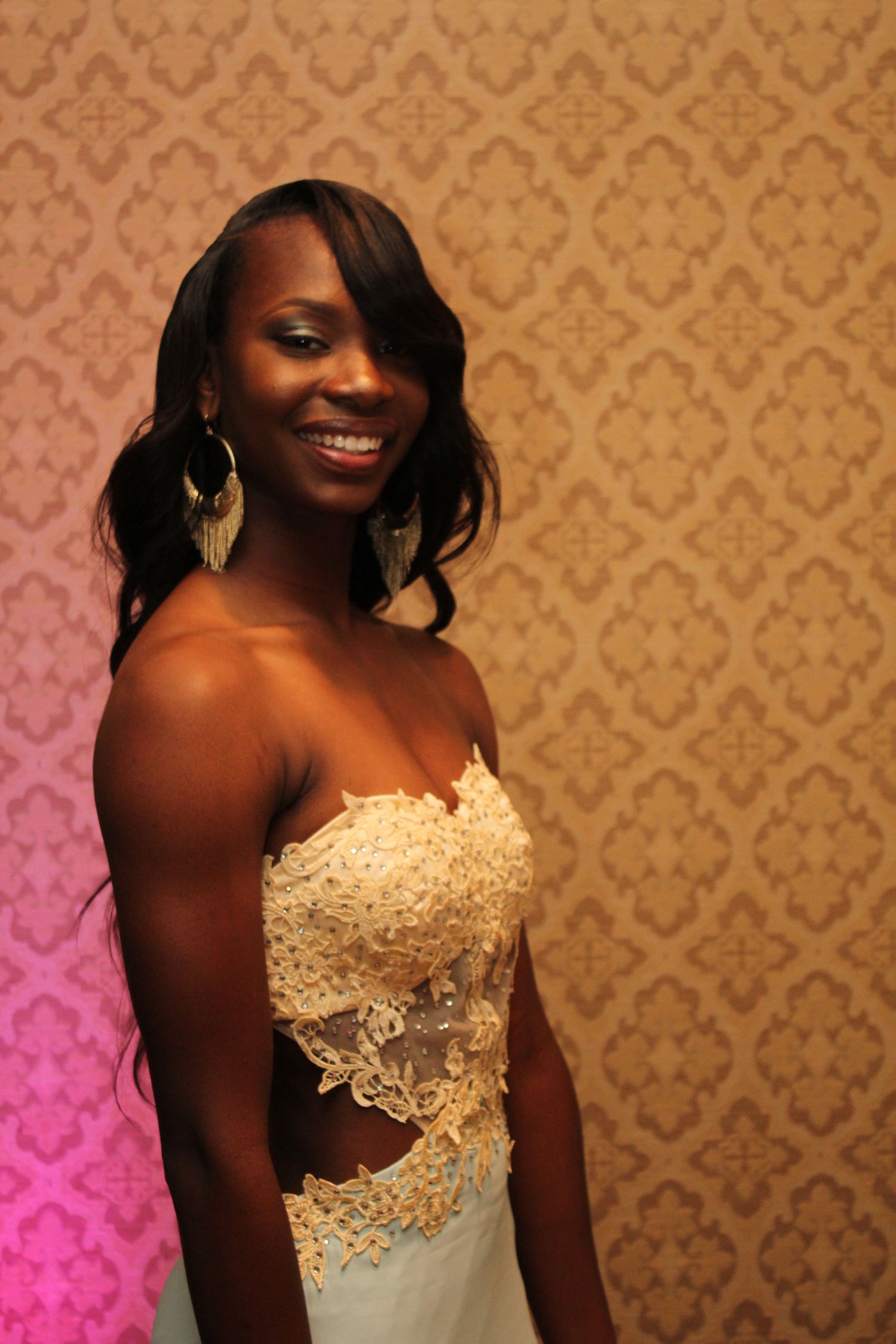 Elegant formal portrait against patterned gold wallpaper wearing white lace gown.