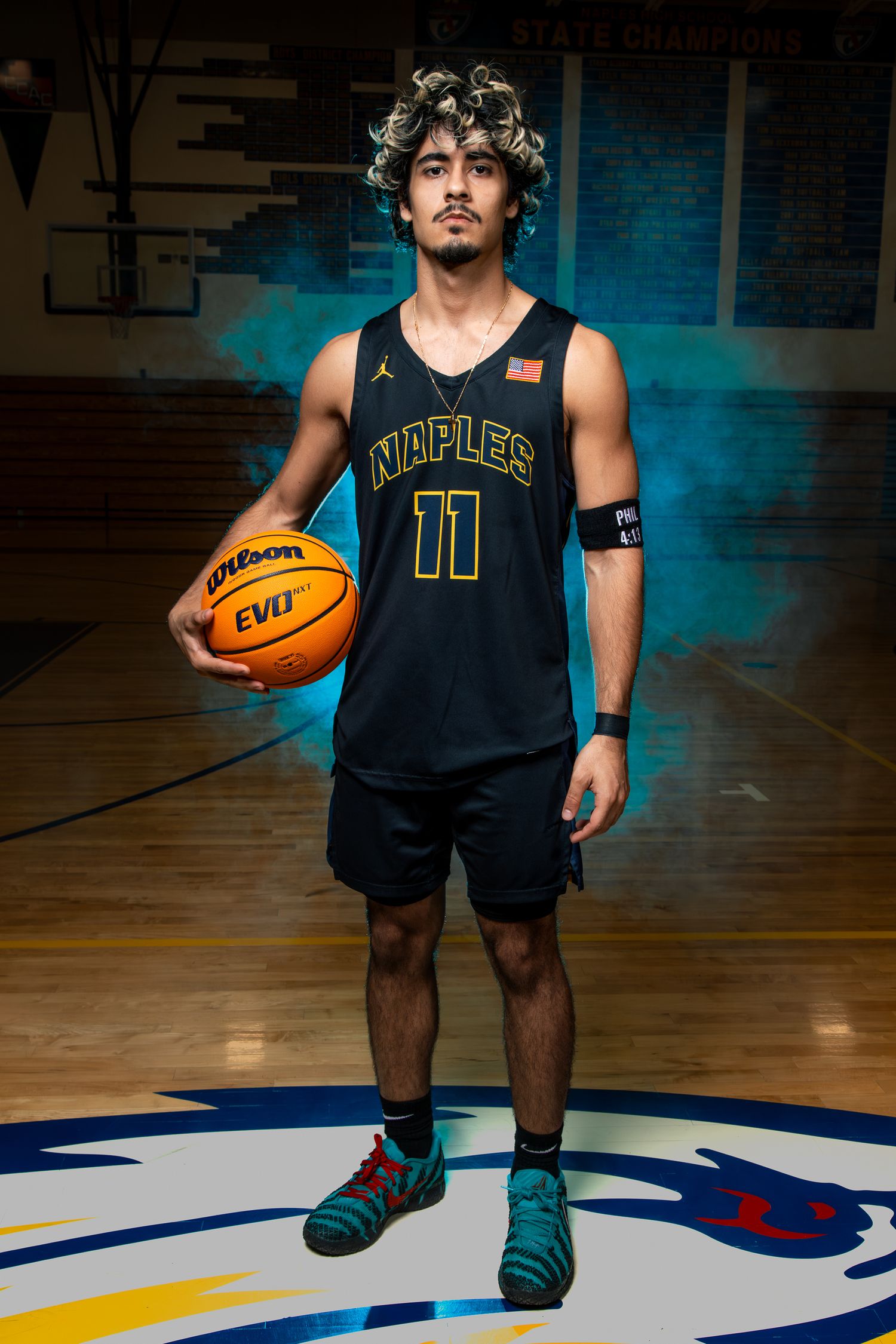 Basketball player in navy uniform dribbles ball on court with dramatic blue lighting and shadows.