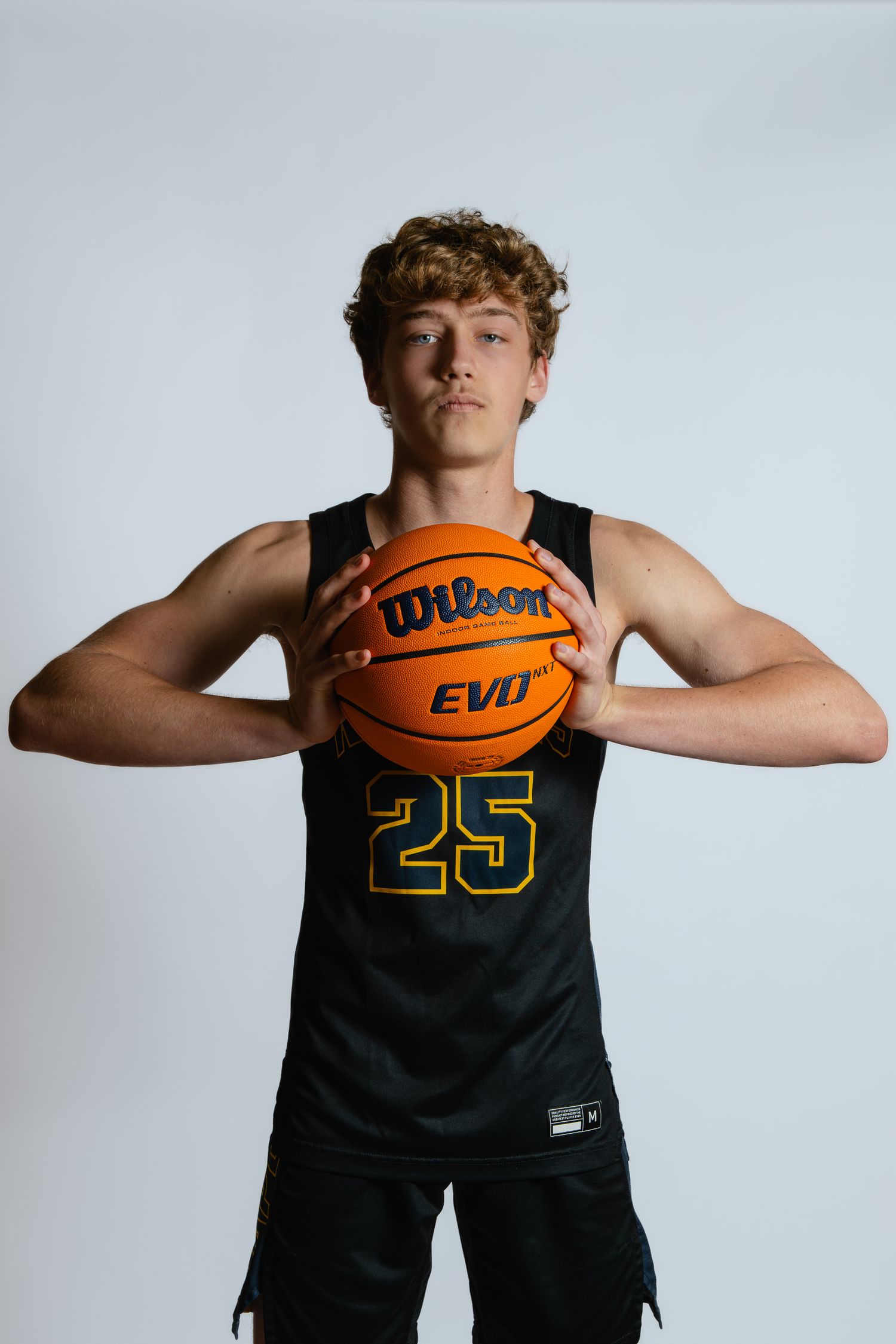 Basketball player in black jersey number 25 poses with orange Wilson ball against white background.