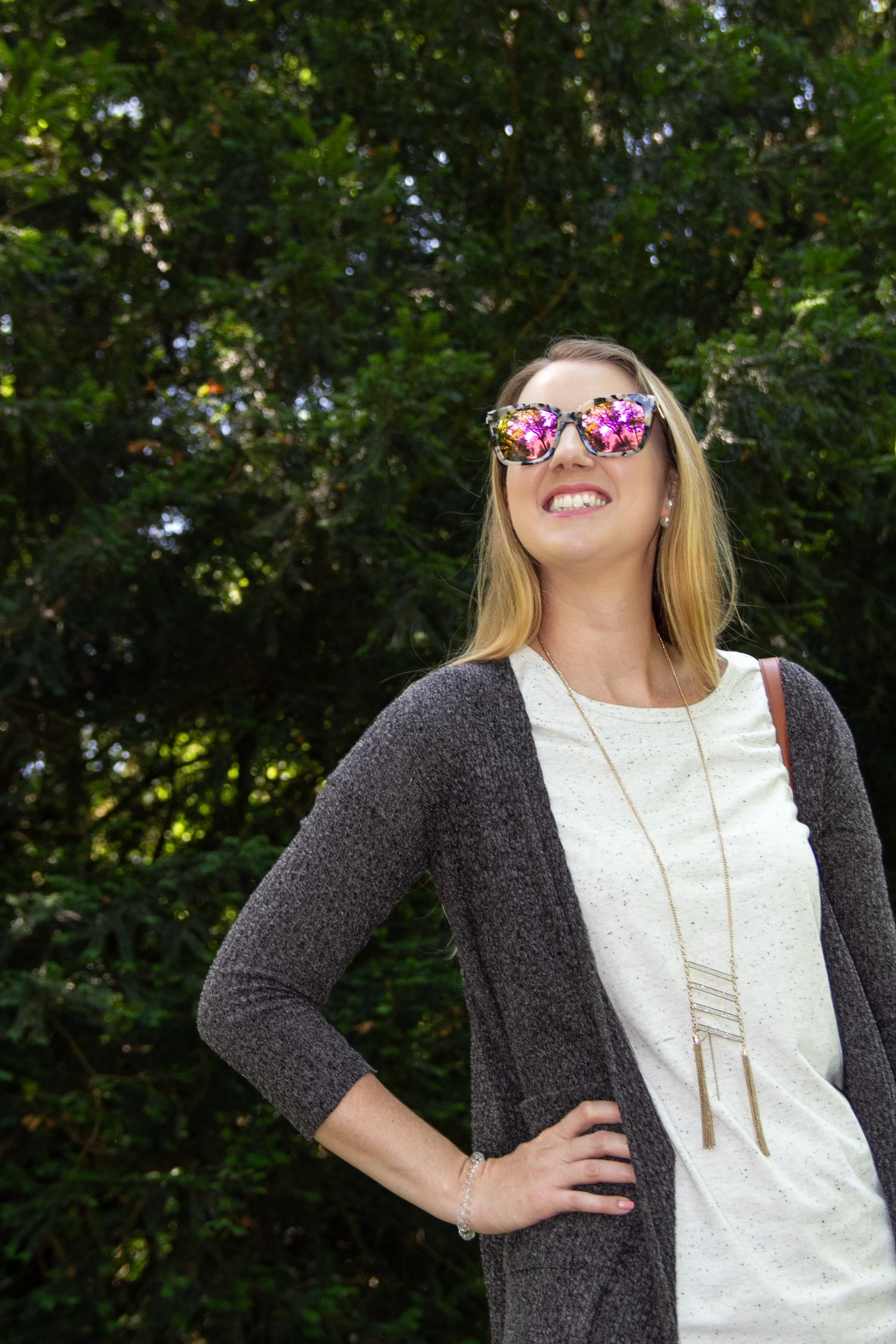 A person wearing a gray cardigan and floral sunglasses laughs joyfully outdoors.