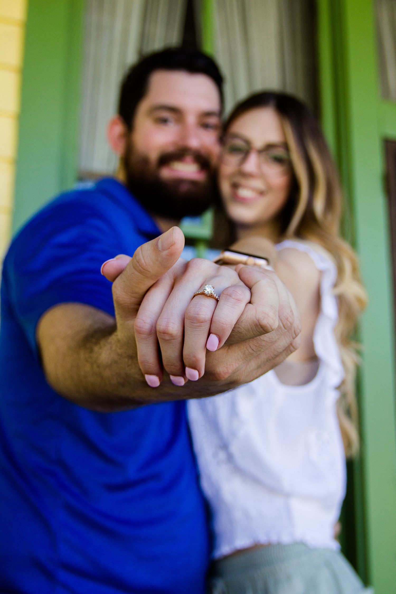 A couple shows off an engagement ring in a close-up shot highlighting their joined hands.