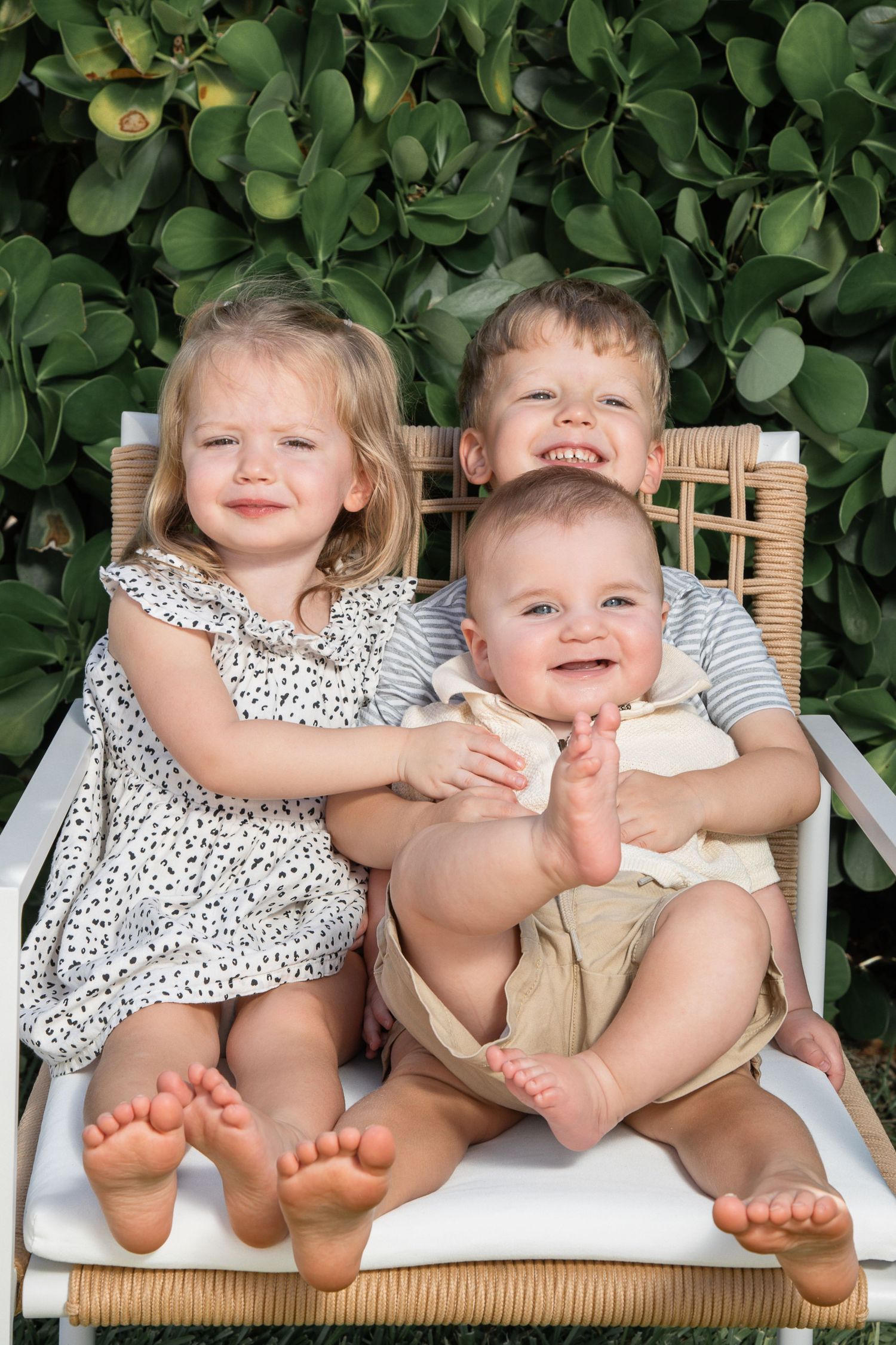 Two young children sitting on a wicker chair showing their bare feet and sharing playful moments together.