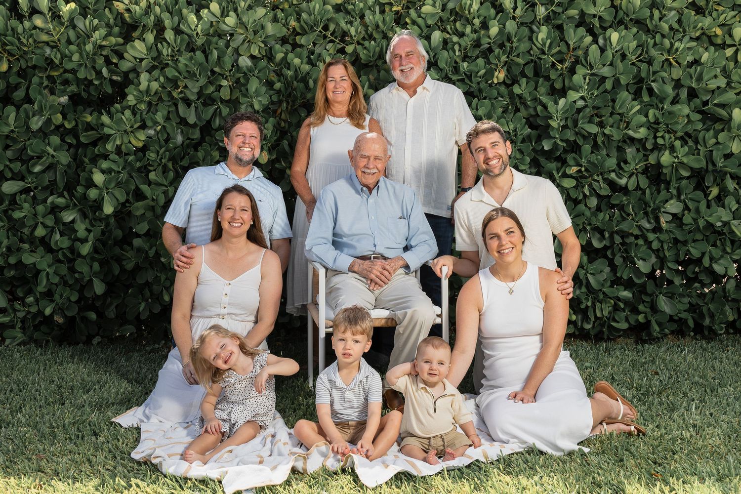 A group wearing coordinated white and blue outfits poses together on grass in front of green hedges.