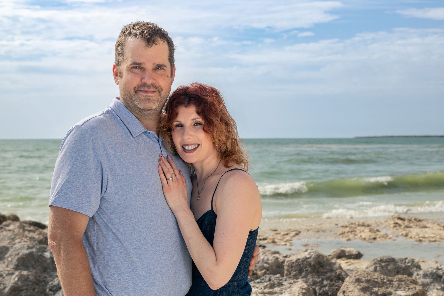 A couple shares a romantic moment along a rocky beach coastline with waves crashing in the background.