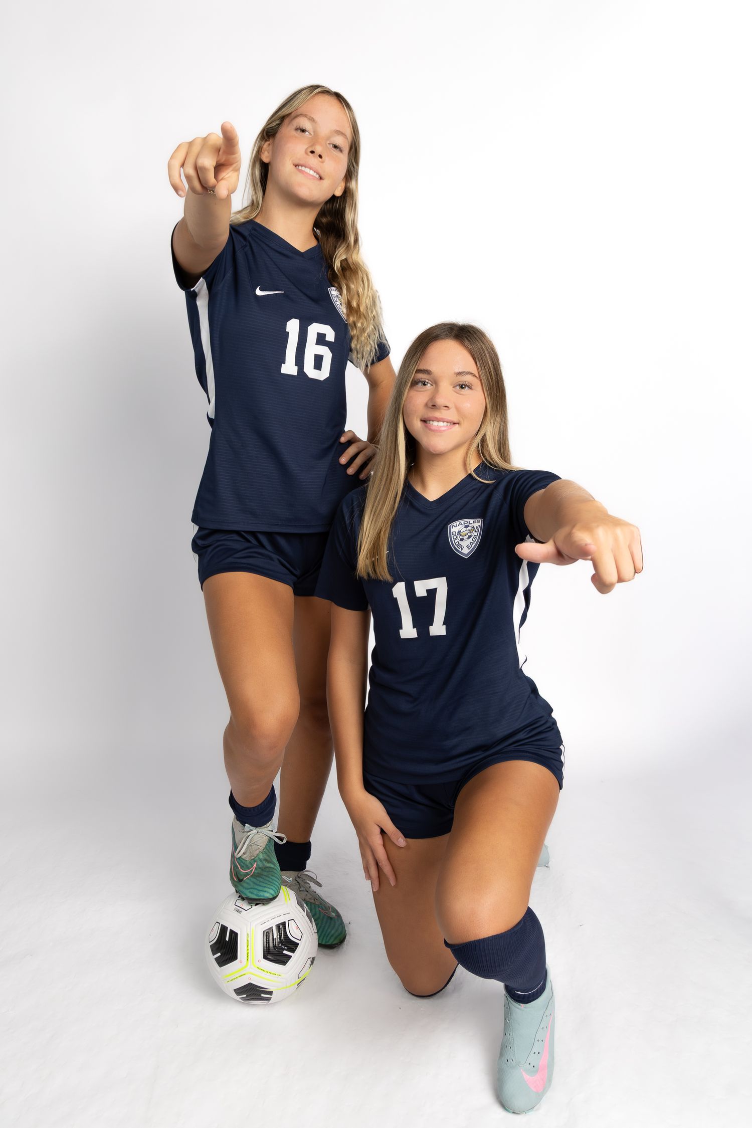 Two soccer players in navy blue uniforms with numbers 16 and 17 pose with a soccer ball in a studio setting.