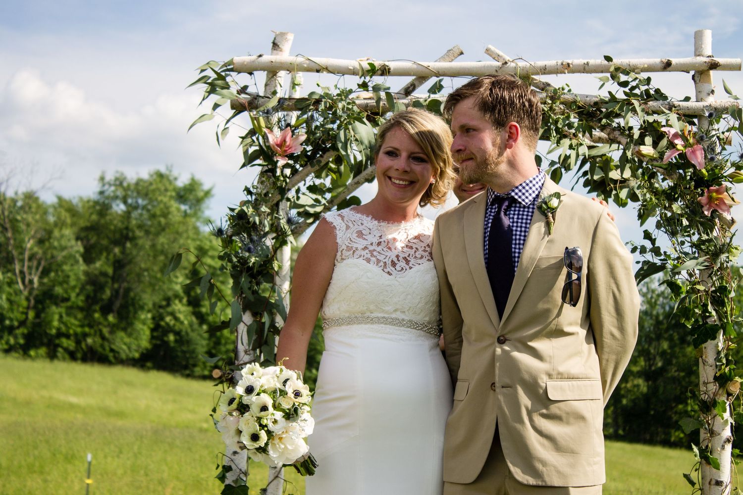 Couple sharing intimate moment under floral arch during outdoor wedding ceremony.
