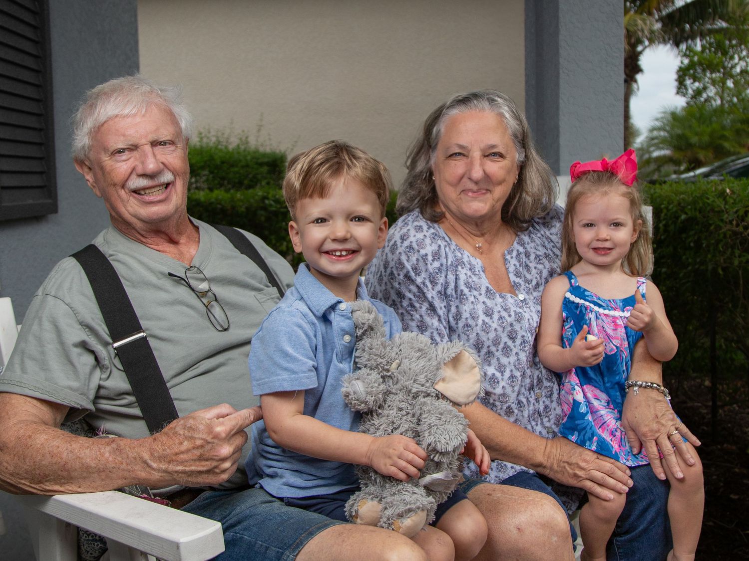 Family members sit together on a porch bench with a stuffed animal.