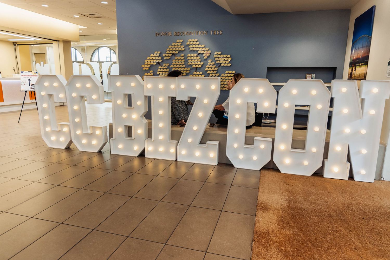 Large illuminated white SHIZ CON letters displayed on tiled floor at event venue.