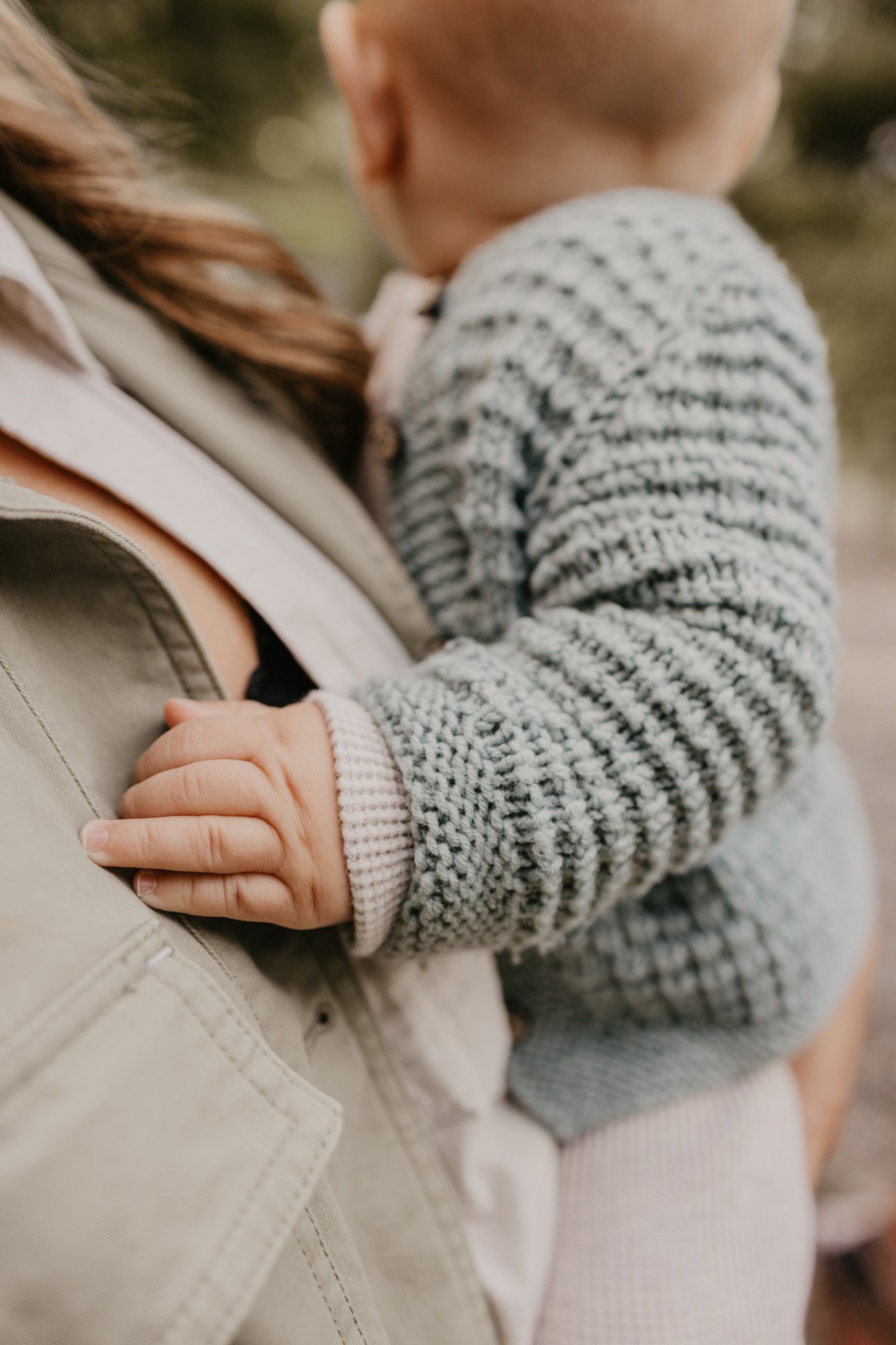 Close-up of baby's hand holding parent's jacket showing knitted gray sweater detail.