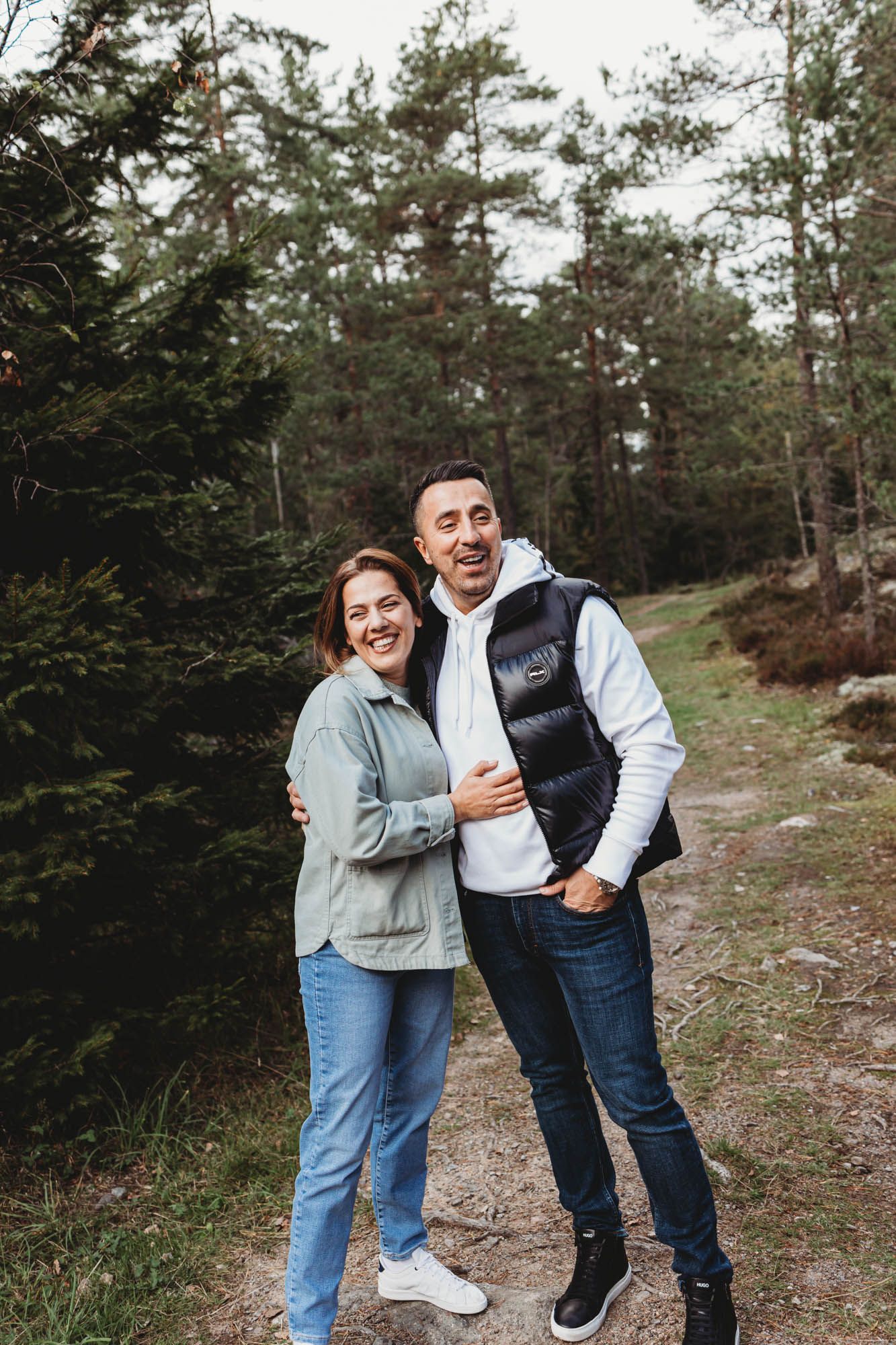 Two people in winter casual wear share a candid moment on forest path.