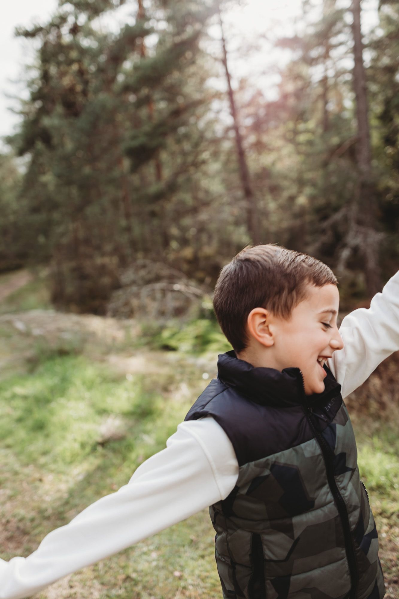 A joyful moment captured in nature wearing a dark puffer vest and white long sleeves.