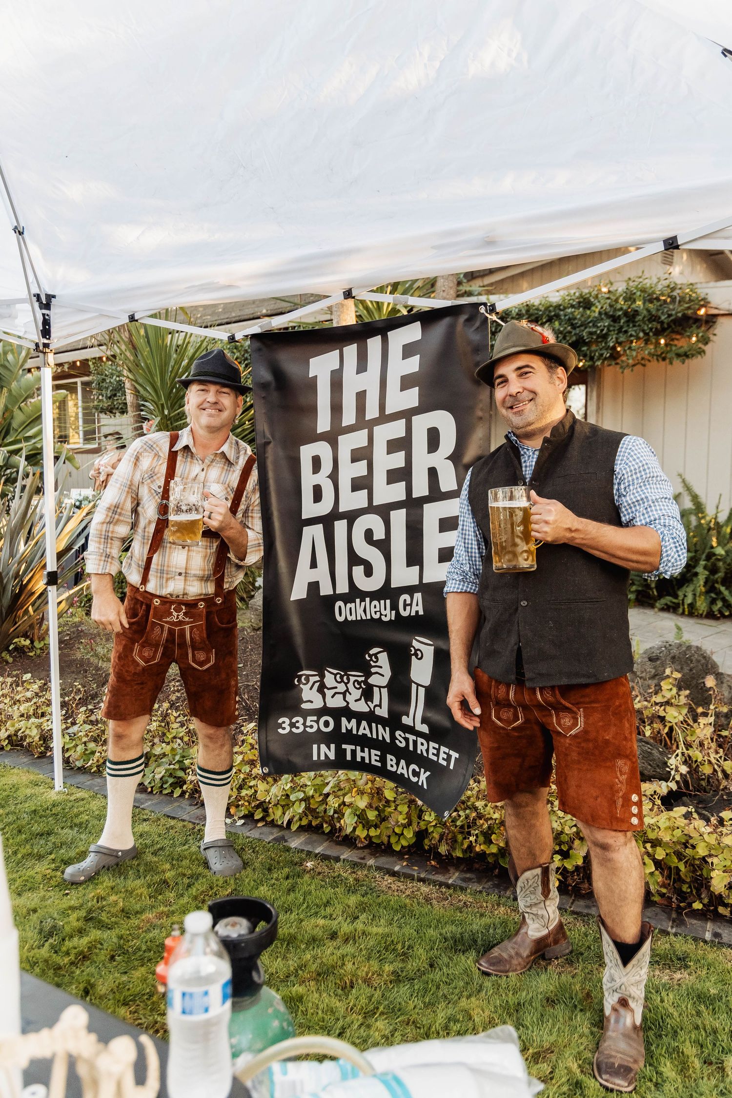 Men in traditional Bavarian lederhosen pose with beer steins in front of The Beer Aisle sign.