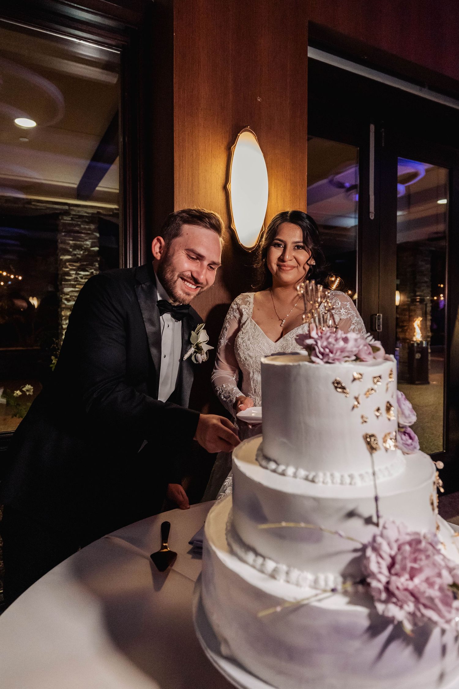 Wedding couple leaning in together over their white tiered cake.