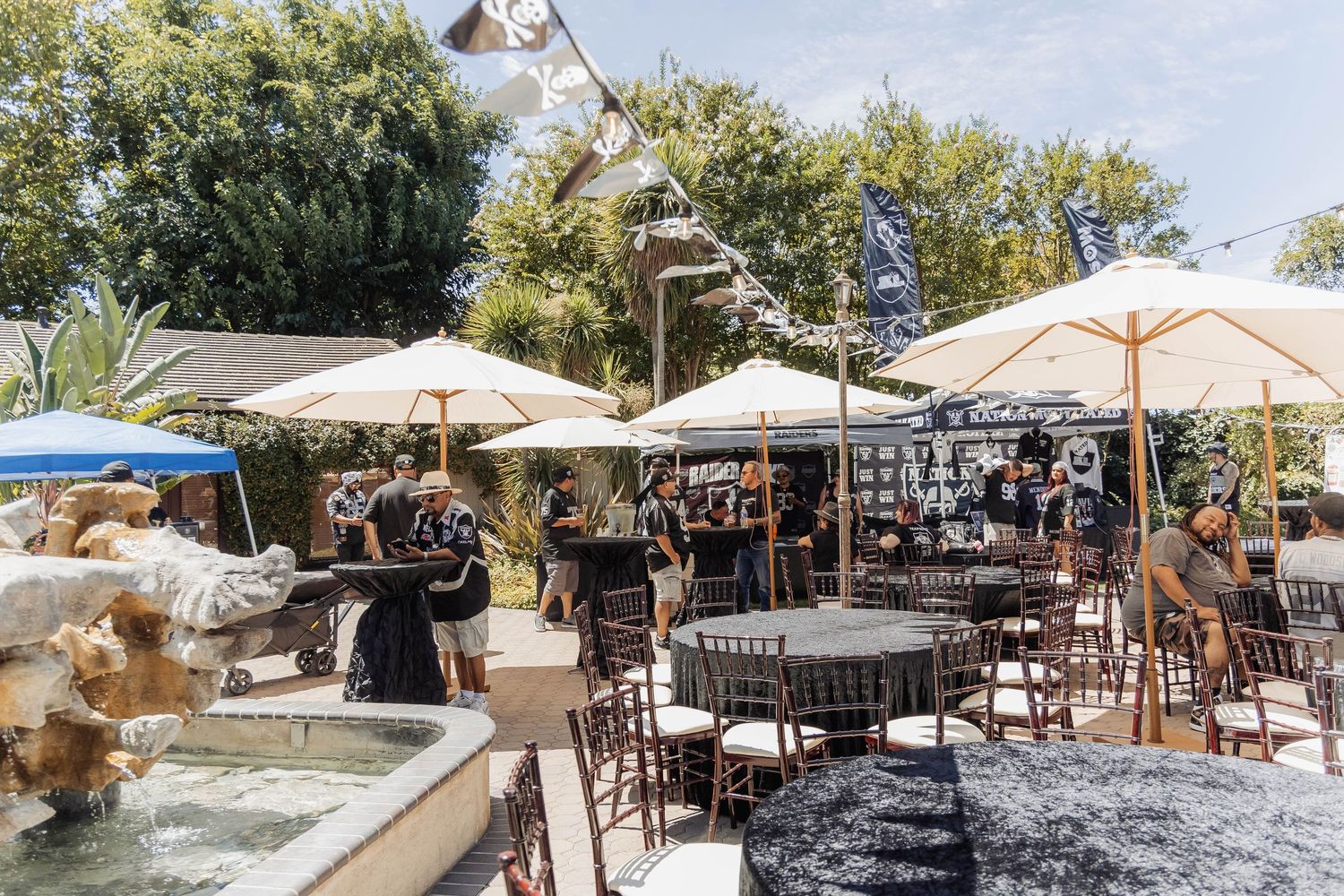 Outdoor patio bar with white umbrellas, round tables, and guests enjoying a sunny day at a casual event venue.